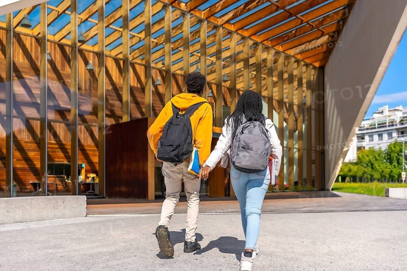 Rear view full length photo of an african young couple walking to university holding hands