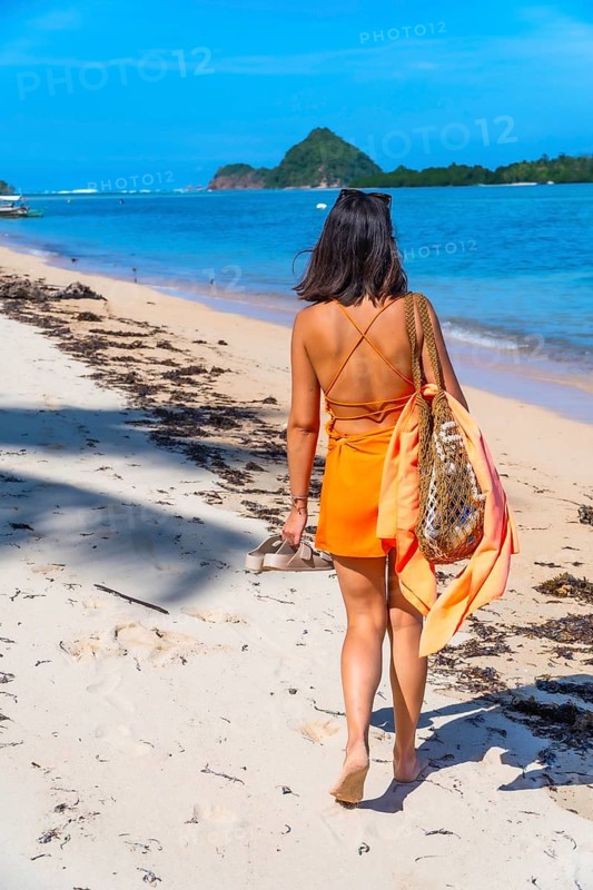 Young woman walking barefoot on white sand at lakdayan beach, coron island, enjoying summer holidays in the philippines