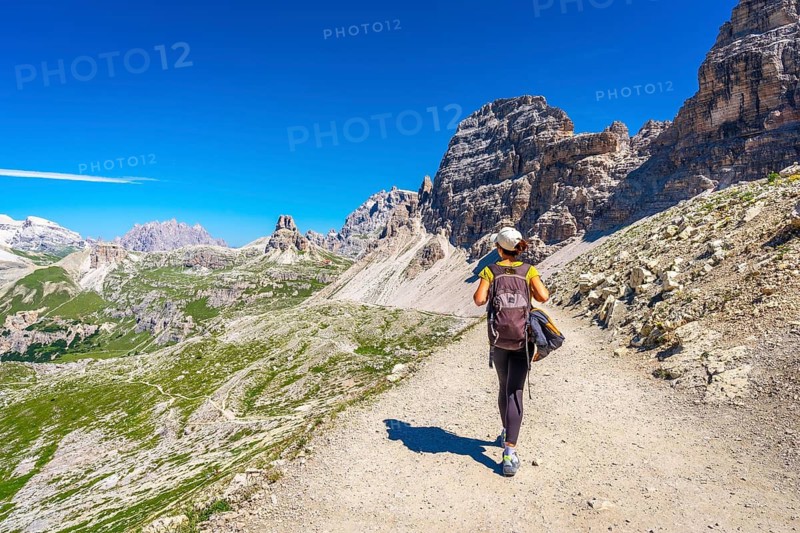 Female hiker walking on a trail in the dolomites mountains with tre cime di lavaredo in the background on a sunny summer day