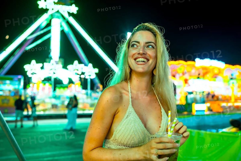 Blonde beauty woman drinking a mojito cocktail in an amusement park at night
