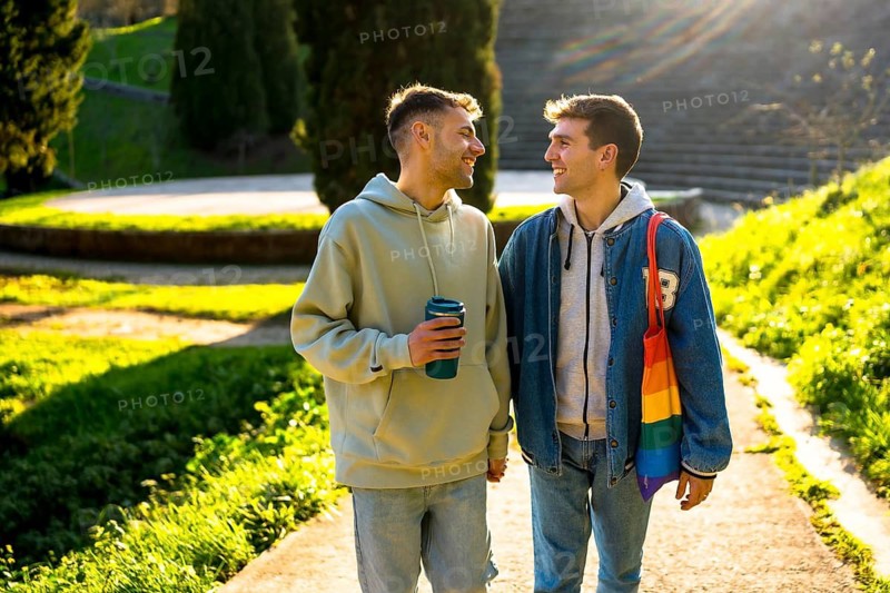Young caucasian gay couple holding hands and walking in a park, enjoying a sunny day together