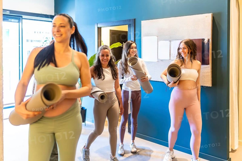 Diverse group of smiling women carrying their yoga mats, walking together and feeling happy after a refreshing fitness and wellness class at a modern studio