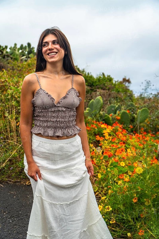 Young woman standing by a path in el hierro, canary islands, smiling and looking away, surrounded by vibrant flowers and green vegetation, enjoying her sunny holiday