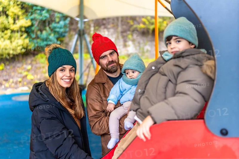 Smiling family enjoying a day at the playground, with children playing on a slide during the fall season