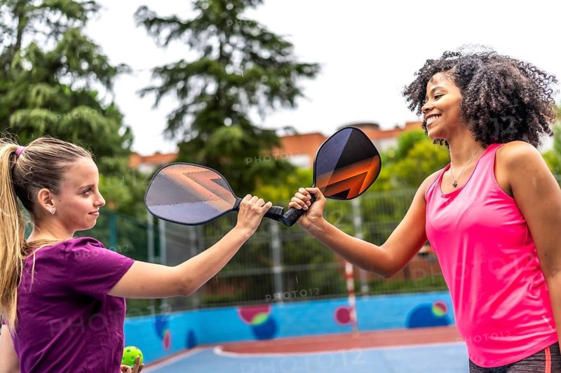Team of two multi-ethnic women clashing rackets before playing pickelball in an outdoor court