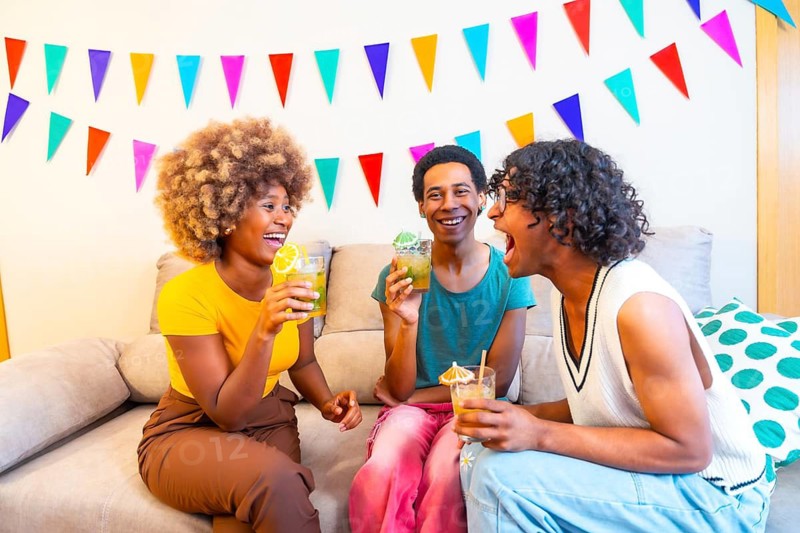 Multi-ethnic friends drinking cocktails on the sofa at a party decorated home