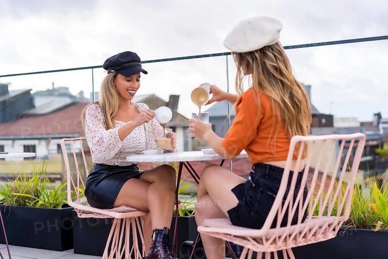 Two blonde stylish women pouring coffee into glasses in an outdoors cafeteria