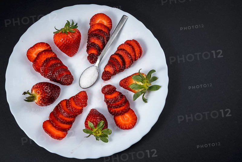 Natural strawberries on a white plate with a spoon of sugar with black background