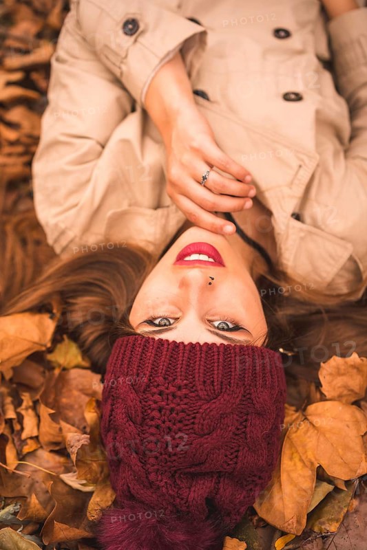 Portrait of a woman in autumn lying on brown leaves in a forest looking at camera