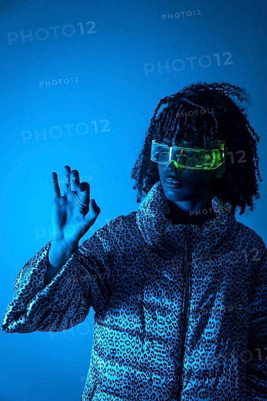 Software engineer wearing futuristic glasses using augmented reality interface making ok sign on blue background