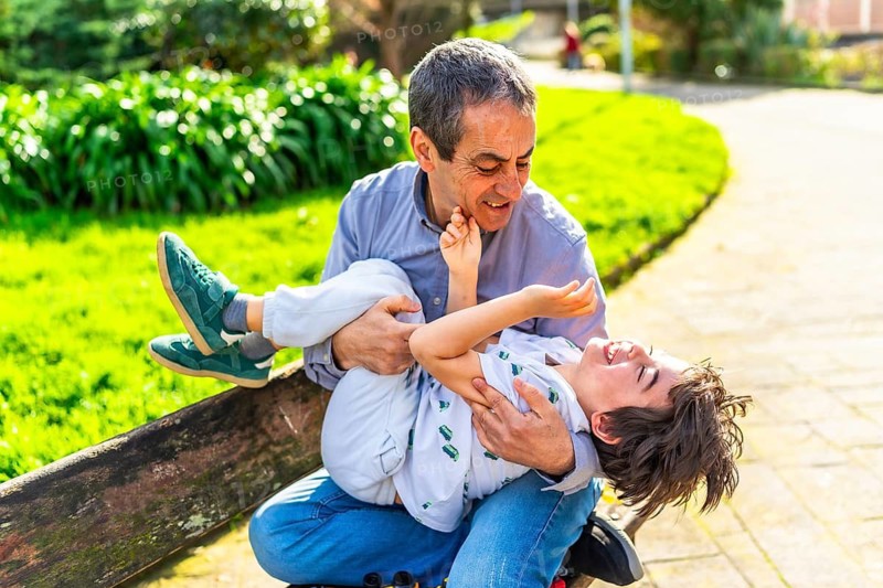 Grandfather and grandson enjoying a playful moment together, sitting on a bench in a sunny park