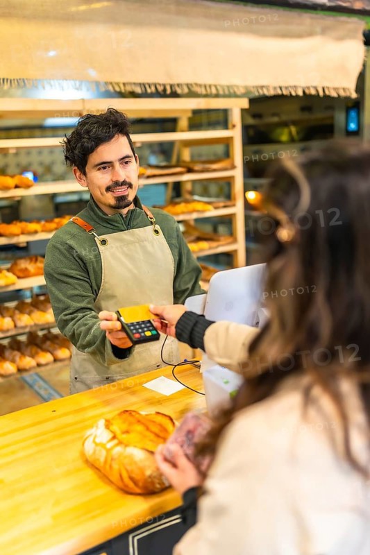 Vertical photo of the rear view of a woman buying bread in a bakery paying with credit card