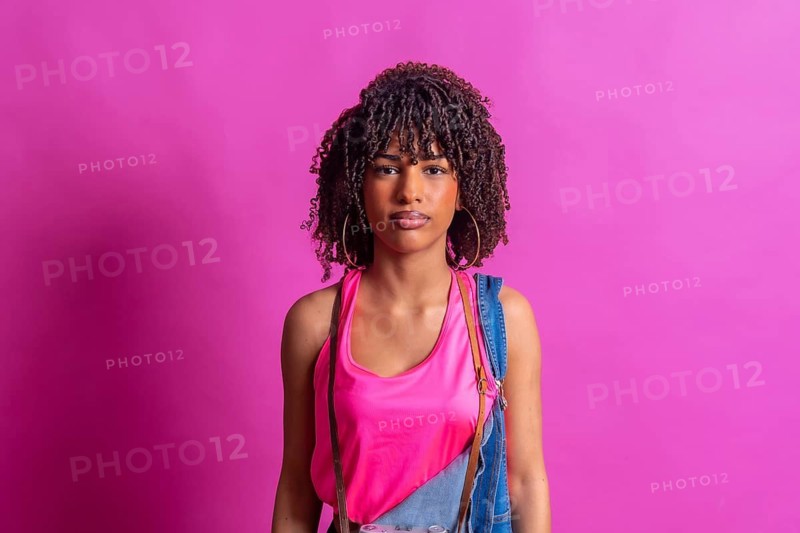Young woman photographer with curly hair posing with vintage camera on pink background, representing creativity, fashion, and youth culture