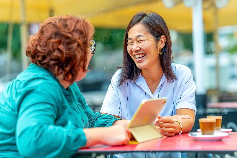 Woman with disability and multi-ethnic friend talking using digital tablet in a sidewalk outdoors cafeteria