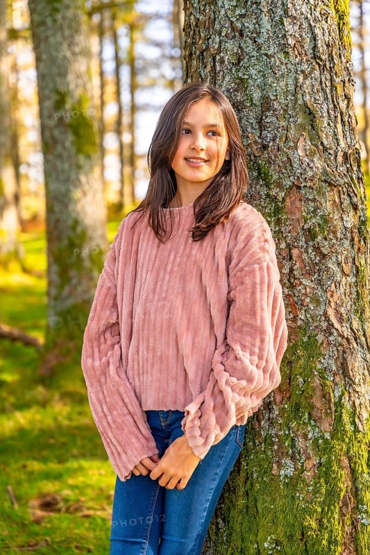 Vertical three quarter length photo of a caucasian Girl leaning relaxed on a tree trunk in the forest