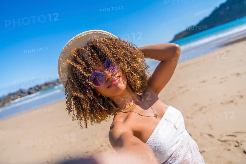 Personal perspective of a beauty brunette woman with curly hair and summer clothes taking selfie at beach