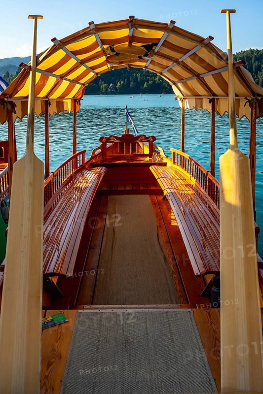 Wooden pletna boat with striped canopy and oars awaits tourists on scenic lake bled in the julian alps, slovenia, a popular summer vacation destination