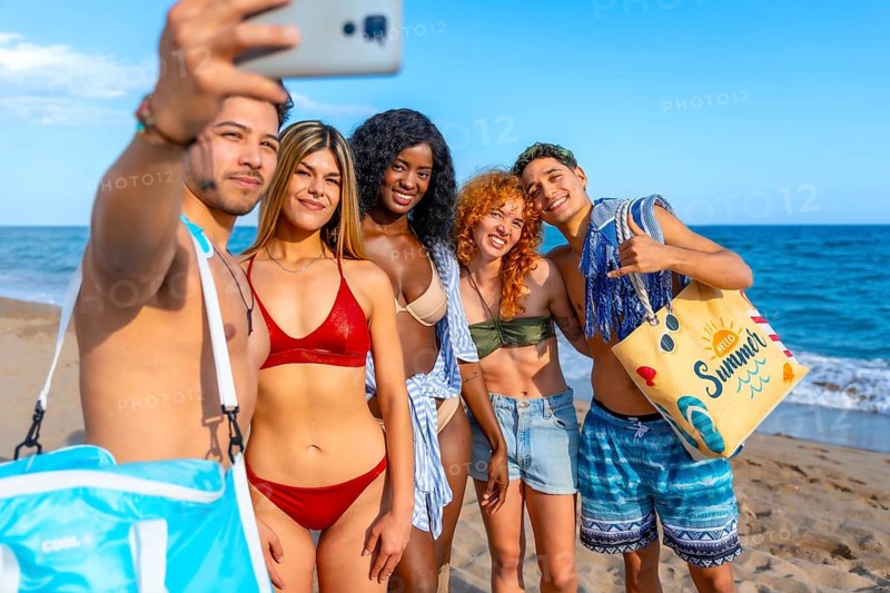 Group of young, multi ethnic friends capturing a joyful selfie on the beach, soaking up the sun and enjoying their summer vacation together