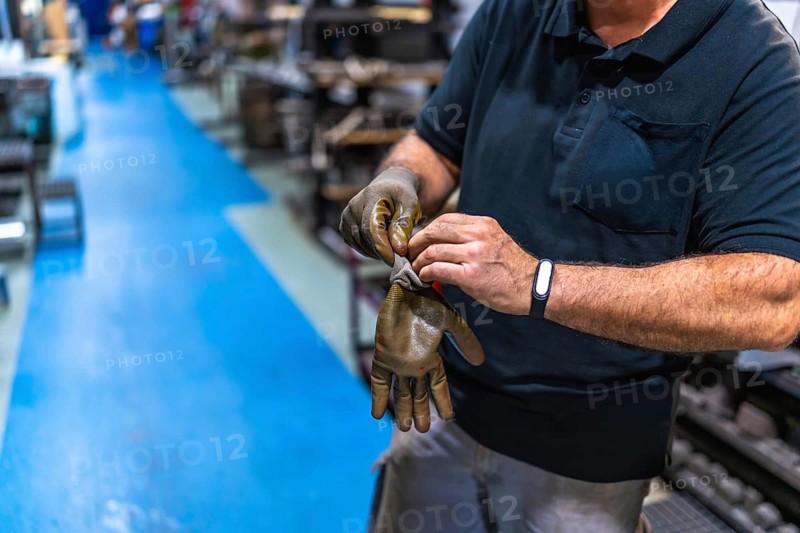 Cropped photo of an unrecognizable mature male caucasian worker putting on protective gloves in a factory