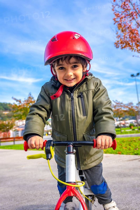 A young boy is riding a bike with a red helmet on. He is smiling and he is enjoying himself
