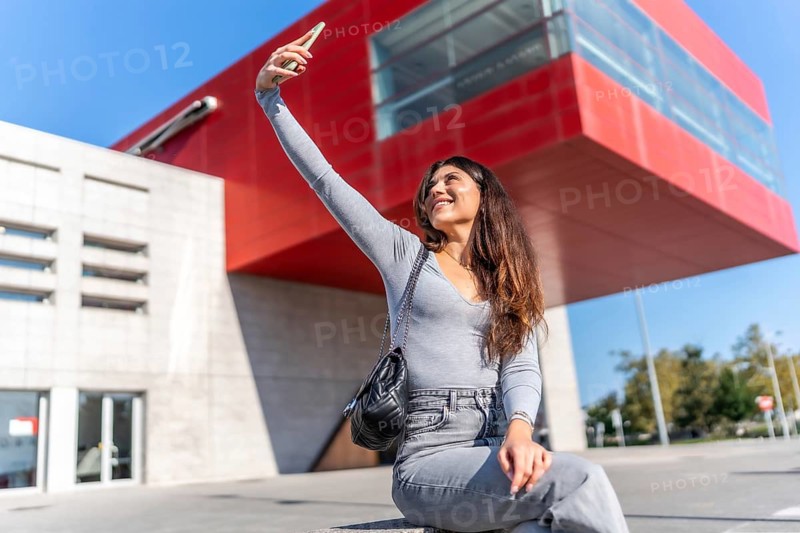 Beauty woman smiling taking a selfie with smartphone sitting on concrete bench in the city