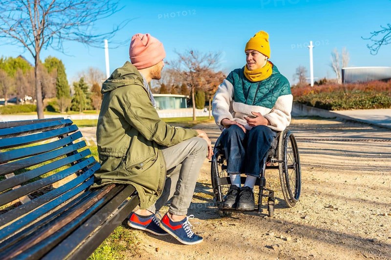 Two young men enjoying conversation on sunny winter day in park, demonstrating inclusion and friendship