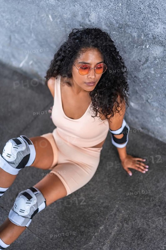 Top view vertical photo of a beautiful latin woman wearing inline roller stake leaning on wall