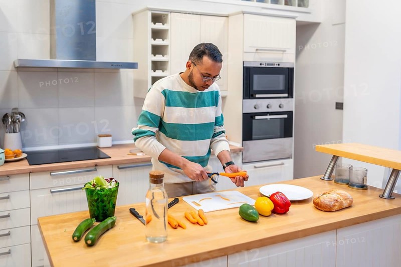 Man peeling a carrot on a cutting board, preparing fresh vegetables for a meal in a modern kitchen, focusing on healthy eating and food preparation lifestyle