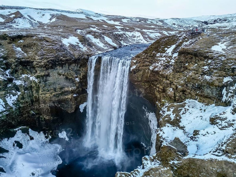 Drone aerial view of Skogafoss waterfall with snow and lots of water in winter in Iceland