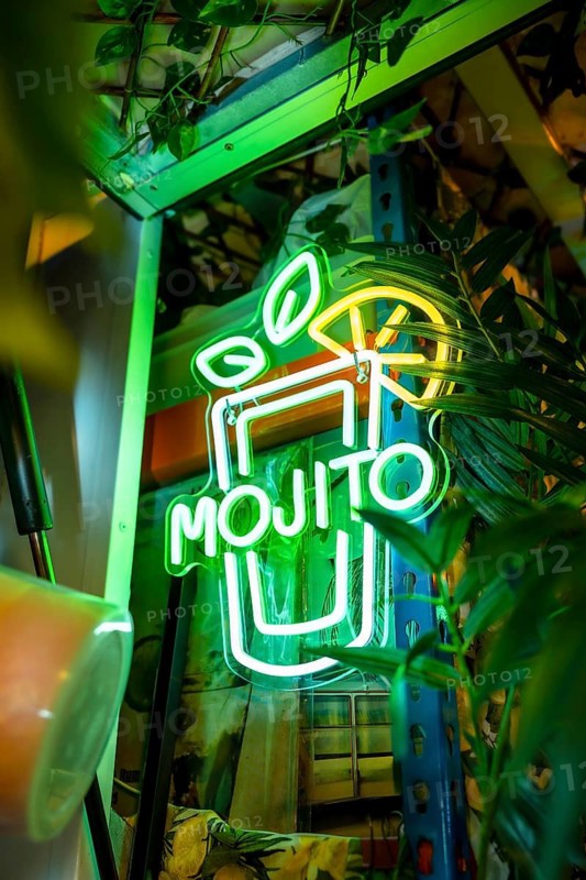 Vertical photo of a mojito cocktail glass in a neon light panel in a bar
