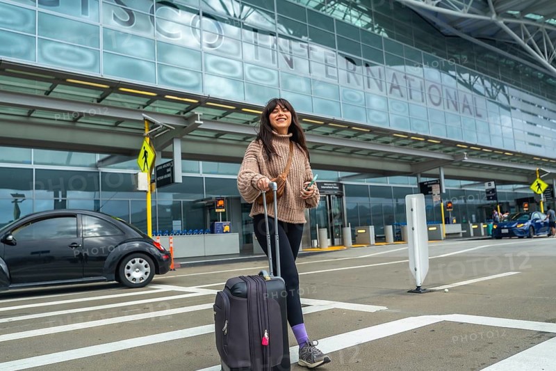 Young woman smiling and pulling luggage, walking from the international terminal building at san francisco international airport, arriving or departing for a journey