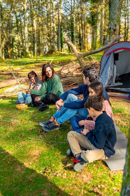 Vertical full length photo of a caucasian family sunbathing enjoying nature during camping weekend in the forest