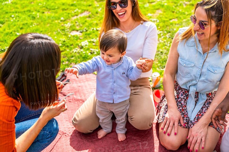 Adorable baby boy learning to walk, supported by family during a cheerful picnic in the park, enjoying quality time together