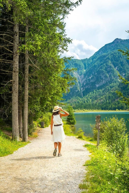 Tourist walking along a gravel path by lake dobbiaco with mountains and pine forest in the background