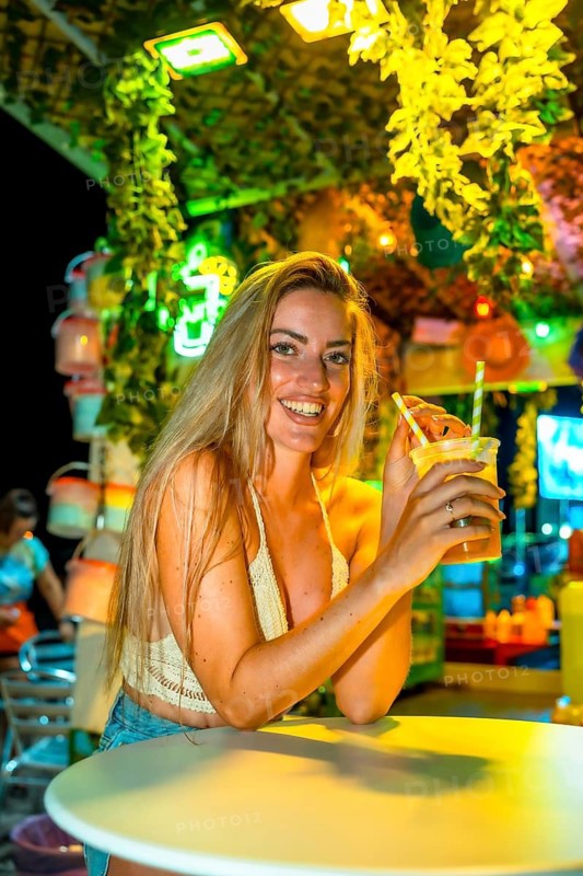 Vertical photo of a blonde woman drinking cocktail enjoying summer night