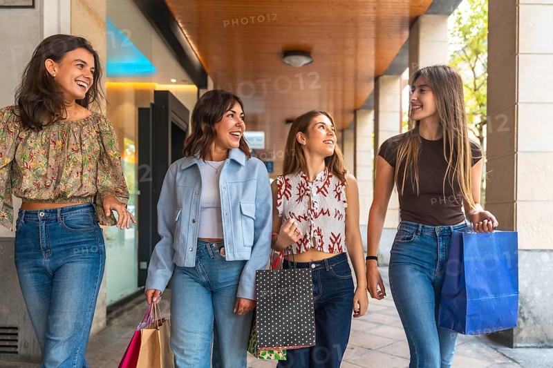 Four young women laughing and walking down a city street with shopping bags, enjoying a casual, stylish weekend outing together cheerful, social, multi ethnic friends having fun