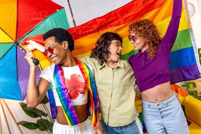 Multi-ethnic friends waving lgbt rainbow flag and dancing partying at home and celebrating pride together