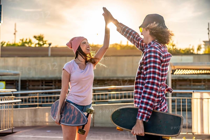 Two young people with skateboards are giving a high five at sunset, expressing joy and camaraderie in an urban setting