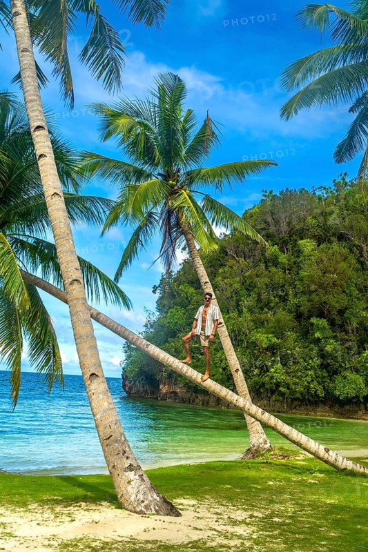 Young man standing on leaning palm trees on a beautiful tropical beach in kangbangyo island, siargao, philippines