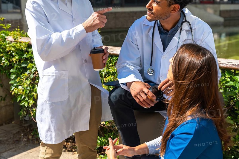 Diverse medical professionals wearing lab coats and scrubs engaging in thoughtful discussion and teamwork during a relaxed coffee break outside the hospital environment