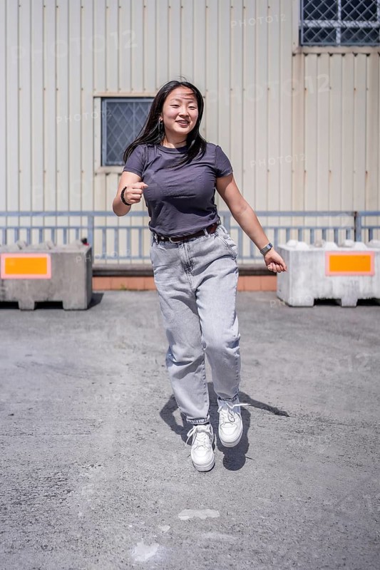 Vertical photo of a female happy young urban korean dancer jumping energetically performing in an industrial space