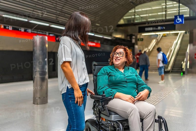 Disabled caucasian smiling woman and asian friend talking waiting in the subway platform