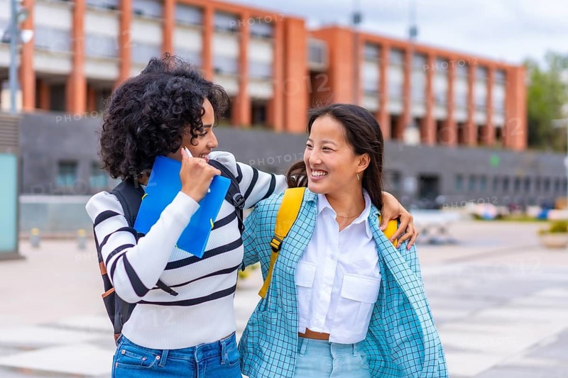 Multi-ethnic female students walking embraced and smiling outside the university campus