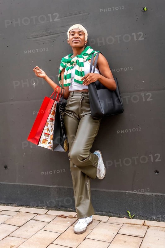 Vertical portrait of a confident african woman leaning on wall carrying shopping bags
