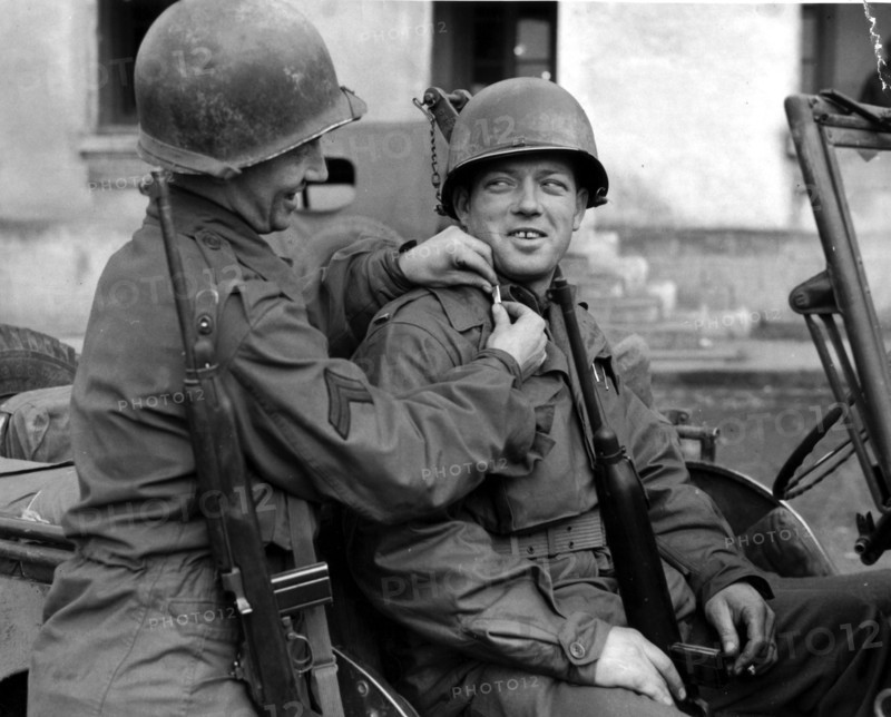 Un caporal américain aide un sous-lieutenant fraîchement nommé à mettre ses galons. (Rambervillers en France, le 2 décembre 1944)