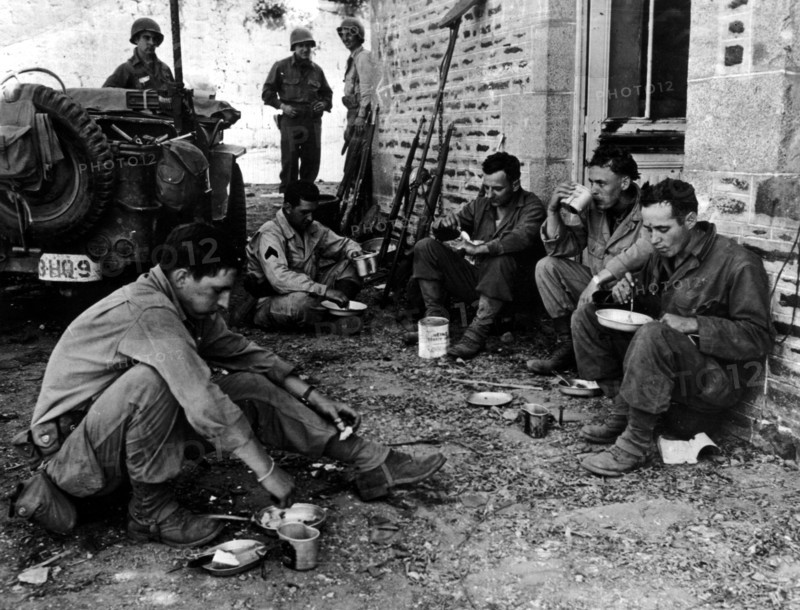 Soldats américains mangeant un repas chaud dans une rue de Perriers.
(Eté 1944)