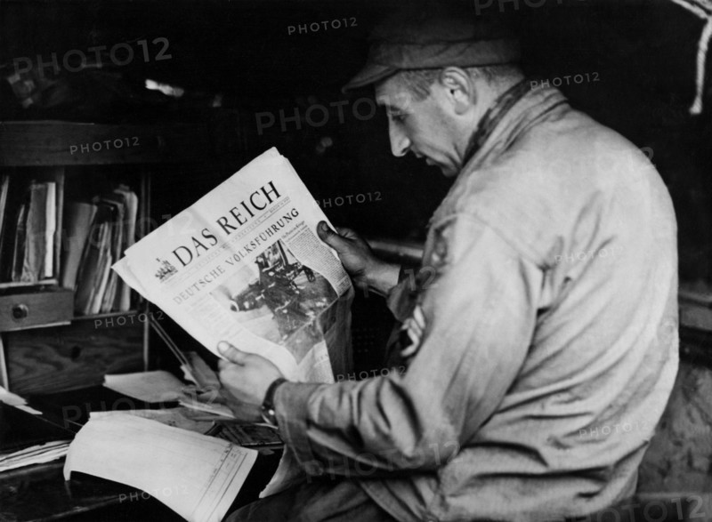 Un soldat américain lit un journal nazi, à Carentan, en Normandie.
 (Juin 1944)