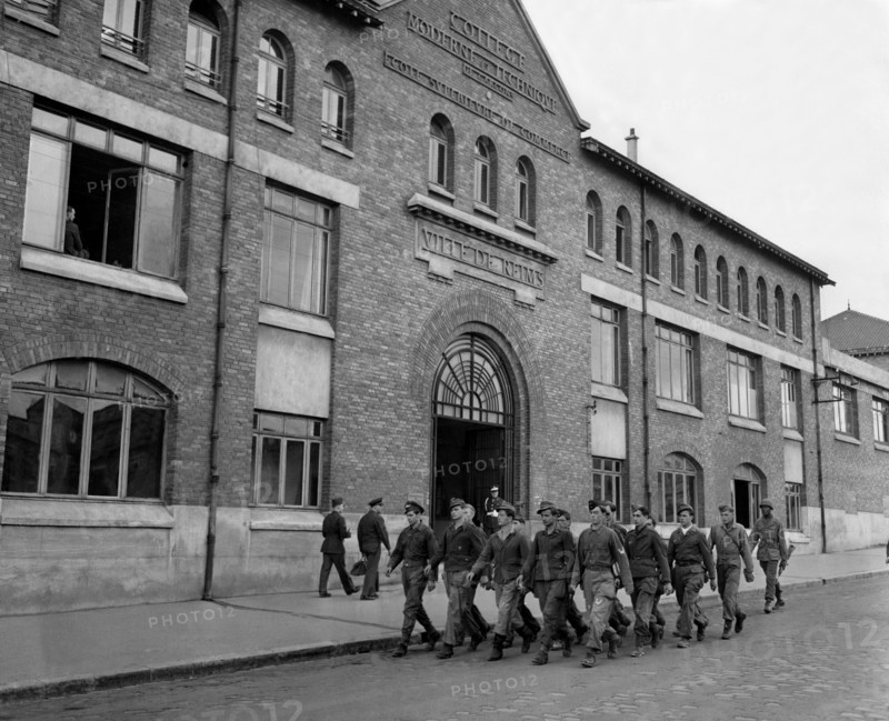 A Reims, des prisonniers de guerre allemands passent devant un établissement scolaire.
(23 mai 1945)