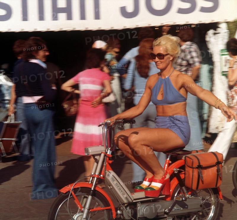 Where the rich and beautiful go on holiday: A woman, lightly dressed for summer and wearing high-fashion shoes with platform soles, rides a moped through St Tropez in France. Taken in 1975.