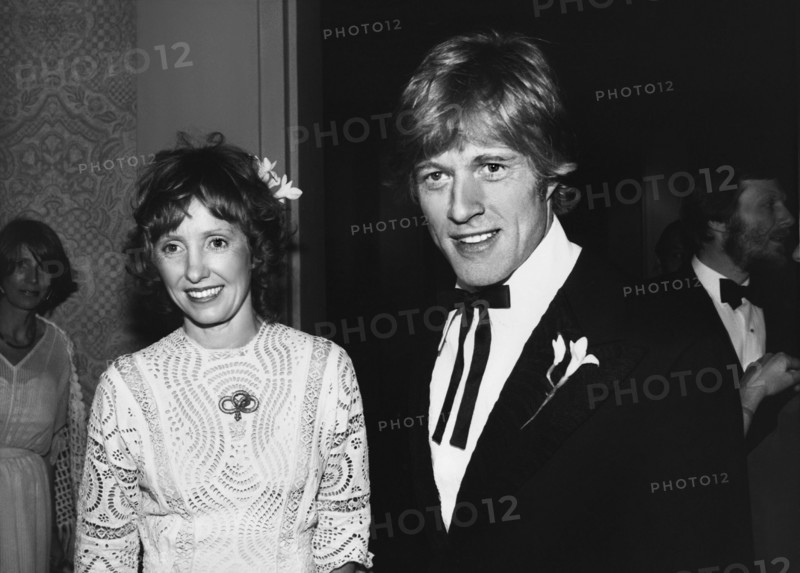 Lola und Robert Redford (Mitte der 1970er Jahre) / Personen, Ehepaar, married, verheiratet, Frau Spitzenkleid, Haarschmuck, Mann Blume am Revers